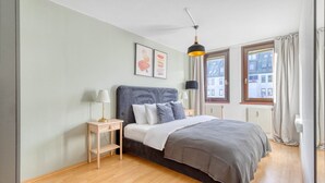 Ein Schlafzimmer mit Bett, Nachttischen, einer Lampe, einem Fenster und Bildern an der Wand.