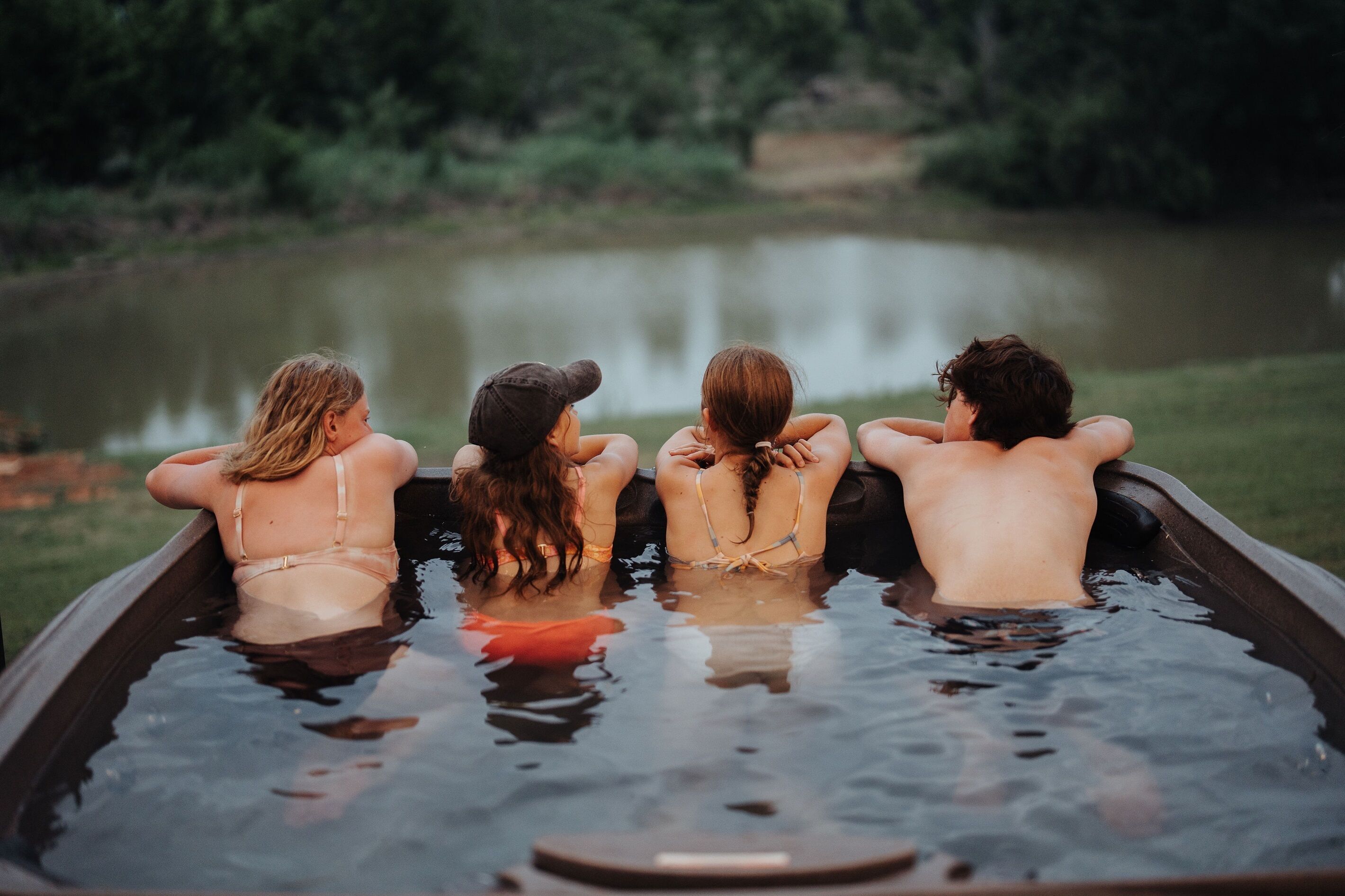 Vier personen zitten in een jacuzzi, met een meer op de achtergrond.