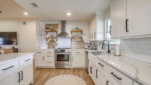 A modern kitchen with white cabinetry, a stainless steel range hood, and a central island. - Lakefront Retreat | Hot Tub + Kayaks | Sleeps 20 (Granbury)