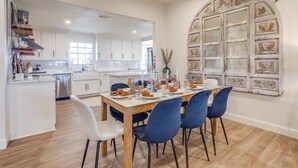 A modern kitchen with white cabinets, a wooden dining table set for four, and a large decorative window with intricate designs. - Lakefront Retreat | Hot Tub + Kayaks | Sleeps 20 (Granbury)