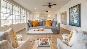 A modern living room with a grey sofa, yellow pillows, a white coffee table, and a ceiling fan. - Lakefront Retreat | Hot Tub + Kayaks | Sleeps 20 (Granbury)