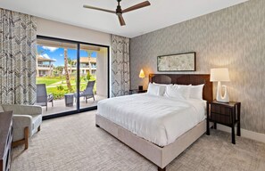Une chambre d’hôtel avec un grand lit, un bureau, une chaise, un ventilateur de plafond, une table de chevet avec une lampe et une vue sur l’extérieur.