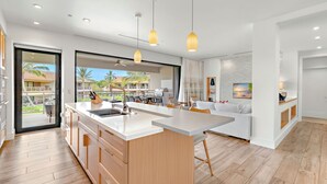 A modern kitchen with a large island, wooden cabinets, and pendant lighting.