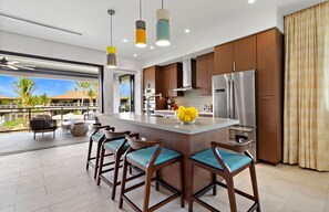 A modern kitchen with a central island, bar stools, and a view of a tropical landscape.