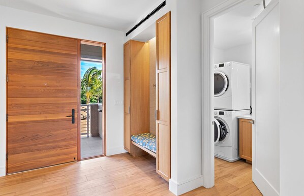 A modern laundry room with a built-in washer and dryer, wooden cabinets, and a bench with a patterned cushion.