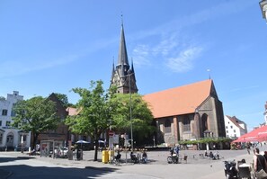 Una plaza con una destacada aguja de iglesia, asientos al aire libre y un cielo azul despejado.