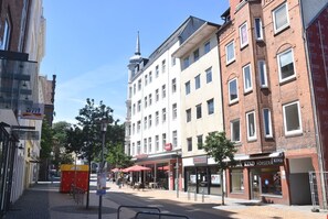 A street view with a mix of modern and traditional buildings, including a prominent white building with a spire.