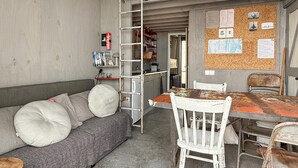 A compact living space with a sofa, a dining table, and chairs. A ladder is leaning against the wall, and a bulletin board with papers and pictures is visible. - 1 bedroom gorgeous home in Vlissingen (Vlissingen)