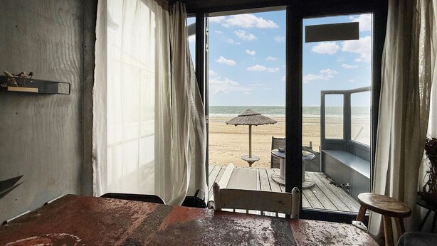 A room with a large window overlooking a beach, a wooden deck outside, and a view of the ocean. - 1 bedroom gorgeous home in Vlissingen (Vlissingen)