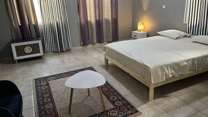 Un dormitorio con cama, mesita de noche, lámpara, cortinas y una silla.