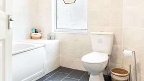 A bathroom with a white toilet, a white bathtub, and a small window with a hexagonal frame.