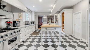 Una cocina con piso a cuadros blanco y negro, muebles blancos, una isla central y una estufa.