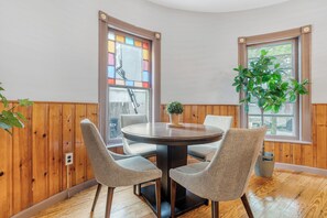 Un comedor con una mesa redonda y cuatro sillas, paredes de paneles de madera, una planta en maceta y una ventana con vistas.