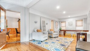 Amplia sala de estar con piso de madera, dos sillones grises con cojines marrones, un tapete colorido y una mesa de centro de madera.