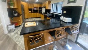 Una cocina moderna con armarios de madera, encimera negra y taburetes de bar.