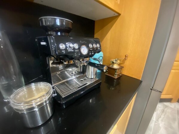 A black espresso machine on a kitchen counter with a stainless steel container and a small decorative item.
