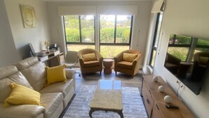 Una sala de estar con un sofá color beige, dos sillones, una mesa de centro y un televisor sobre un mueble de madera.