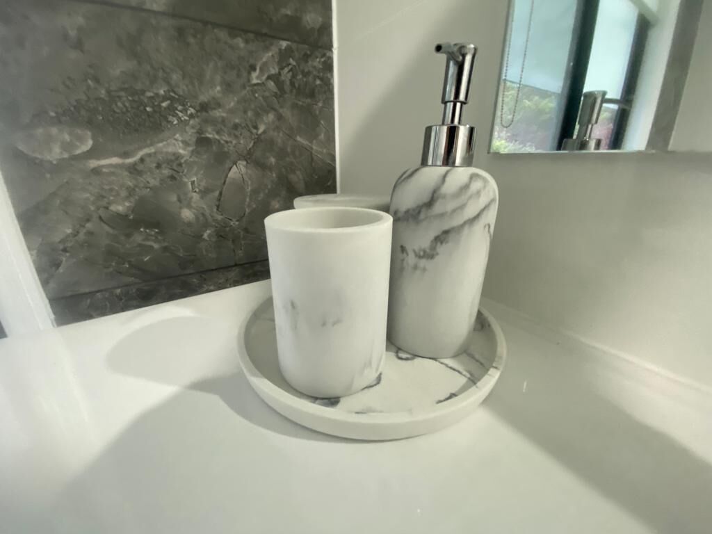 A bathroom vanity with a marble sink, a soap dispenser, and two white cups on a tray.