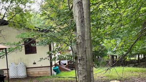 A fire pit with four Adirondack chairs arranged around it, set on gravel with a tree and a building in the background. - Cabin for up to 10 People ! (Tobyhanna)