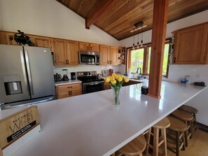 Enjoy cooking in this kitchen with a large island, bar stools, stainless steel appliances, and wooden cabinets.