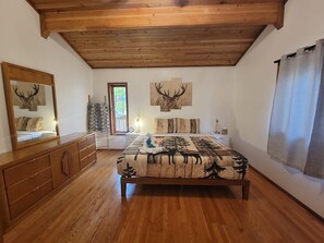 Cozy retreat with a large bed, wooden dresser, and bedside table, set against a white backdrop with deer antler artwork.