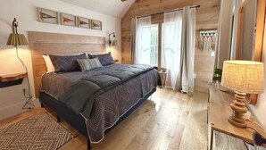 Un dormitorio con techo de madera, una cama con ropa de cama estampada, una lámpara de noche y una ventana con cortinas.