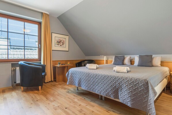 A bedroom with a bed, a chair, a small table, a window, and a radiator.