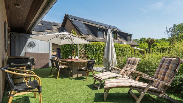 Eine Terrasse mit Tisch, Stühlen und Grillplatz.