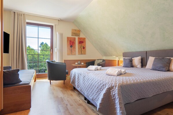 A bedroom with a large bed, a chair, a desk, and a window with curtains.