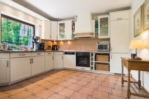 Una cocina con armarios blancos, lavavajillas, horno, microondas y ventana con vistas a zonas verdes.