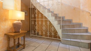 Eine Treppe mit schmiedeeisernem Geländer, ein Holztisch mit Lampe und ein Fliesenboden.
