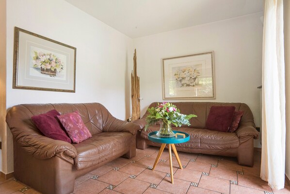 A living room with two brown leather sofas, a blue side table with a vase of flowers, and two framed floral paintings on the walls.