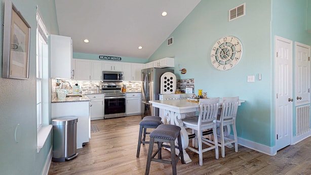 Una cocina con armarios blancos, un refrigerador de acero inoxidable, un microondas y un comedor con una mesa y sillas blancas.