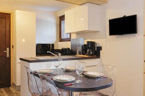 Une cuisine de taille réduite avec des meubles blancs, un plan de travail noir et un téléviseur à écran plat fixé au mur.