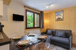A dining area with a table set for four, a sofa, a TV mounted on the wall, and a poster of Mont Blanc. - Hameau Des Grands Montets - Apartment 127, Argentière (Chamonix), France (Argentière (Chamonix))