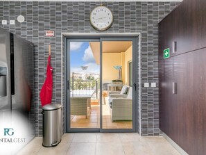 L’entrée moderne d’un hôtel, avec une horloge, un sac rouge accroché au mur et une vue sur l’espace extérieur aménagé en terrasse.