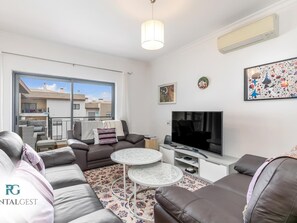 A modern living room with a sofa, a coffee table, a TV, and a balcony with a view of buildings.