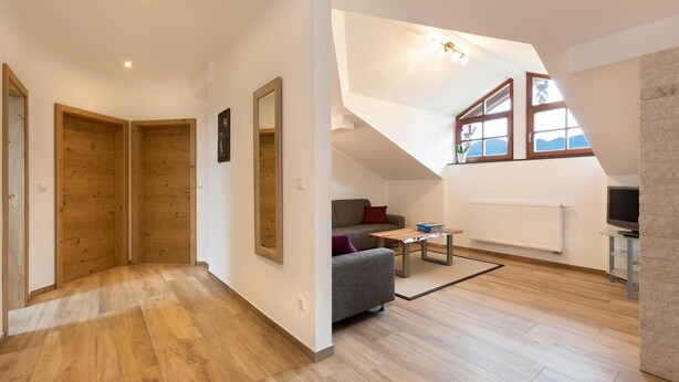 A spacious living area with a high ceiling, wooden flooring, a grey sofa, a small table, and a TV. - Ferienwohnung Nummer 2 im Zweiten Stock (Übersee)