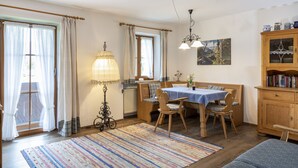 Ein gemütliches Zimmer mit einem Holzesstisch, Stühlen, einem gemusterten Teppich, einer Couch und einem Bücherregal.