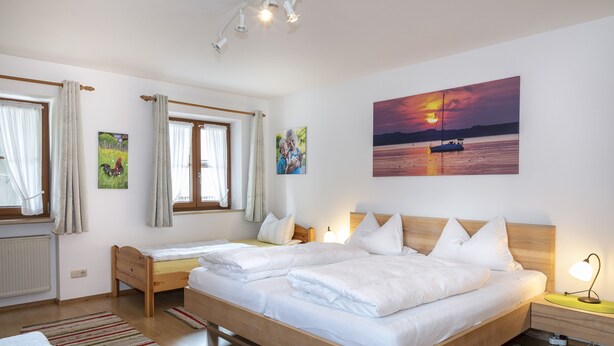 Ein Schlafzimmer mit einem großen Bett, zwei Nachttischen, einem Beistelltisch, einem Fenster mit Vorhängen und einem Gemälde, das einen Sonnenuntergang über Wasser zeigt.