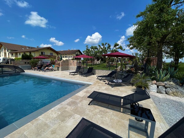 A pool area with lounge chairs and umbrellas, a clear blue sky, and a house in the background.