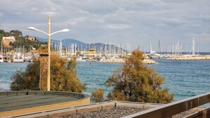 A marina with boats, a street lamp, and a rocky island with trees. - Le Lavandou, Cabin studio to rent for 4 people, sea view, direct access to the beach (LE LAVANDOU)