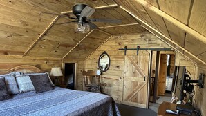 A cozy attic bedroom with a bed, a chair, a desk, and a ceiling fan. - Historic Log Cabin in Greer, AZ.  Located near Molly Butler's & Sunrise Ski Area (Greer)