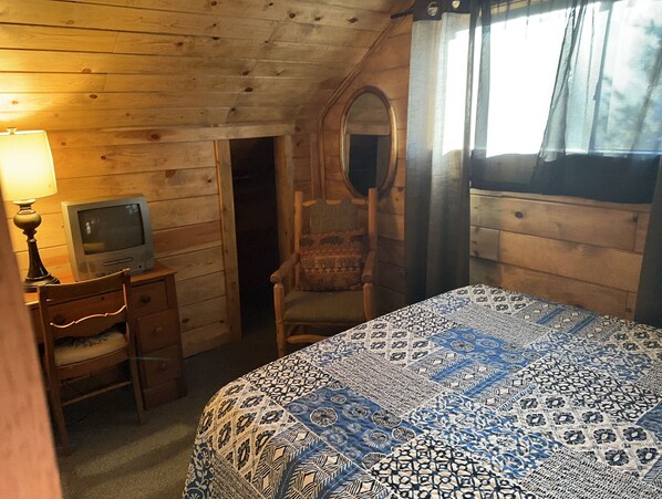 A room with a bed, a chair, a desk, a television, and a mirror. - Historic Log Cabin in Greer, AZ. Located near Molly Butler's & Sunrise Ski Area (Greer)