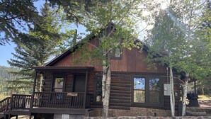 A rustic cabin with a wooden deck and stone foundation, surrounded by trees. - Historic Log Cabin in Greer, AZ.  Located near Molly Butler's & Sunrise Ski Area (Greer)