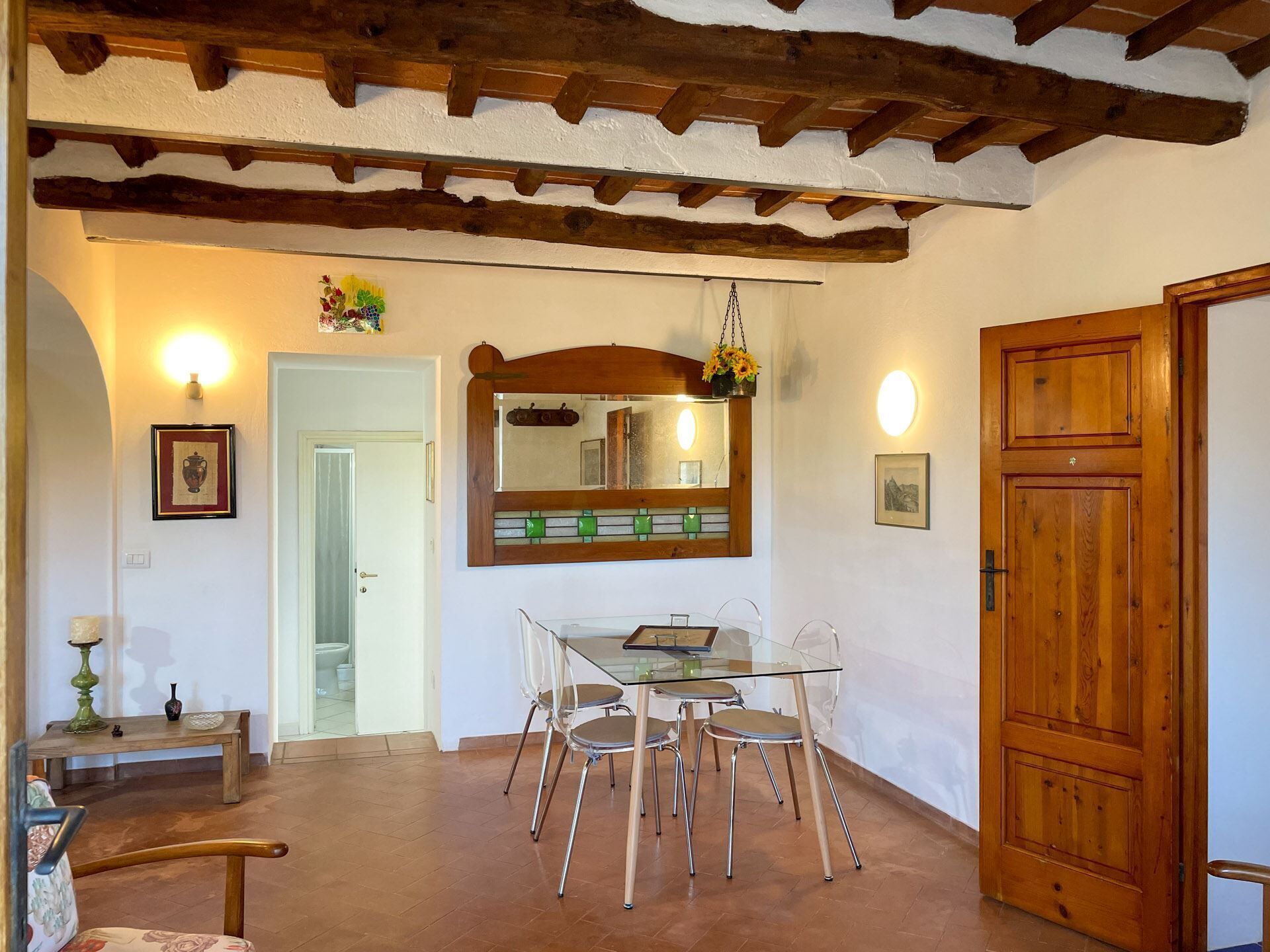 A dining area with a glass table and chairs, a wooden ceiling, and a large mirror above the table.