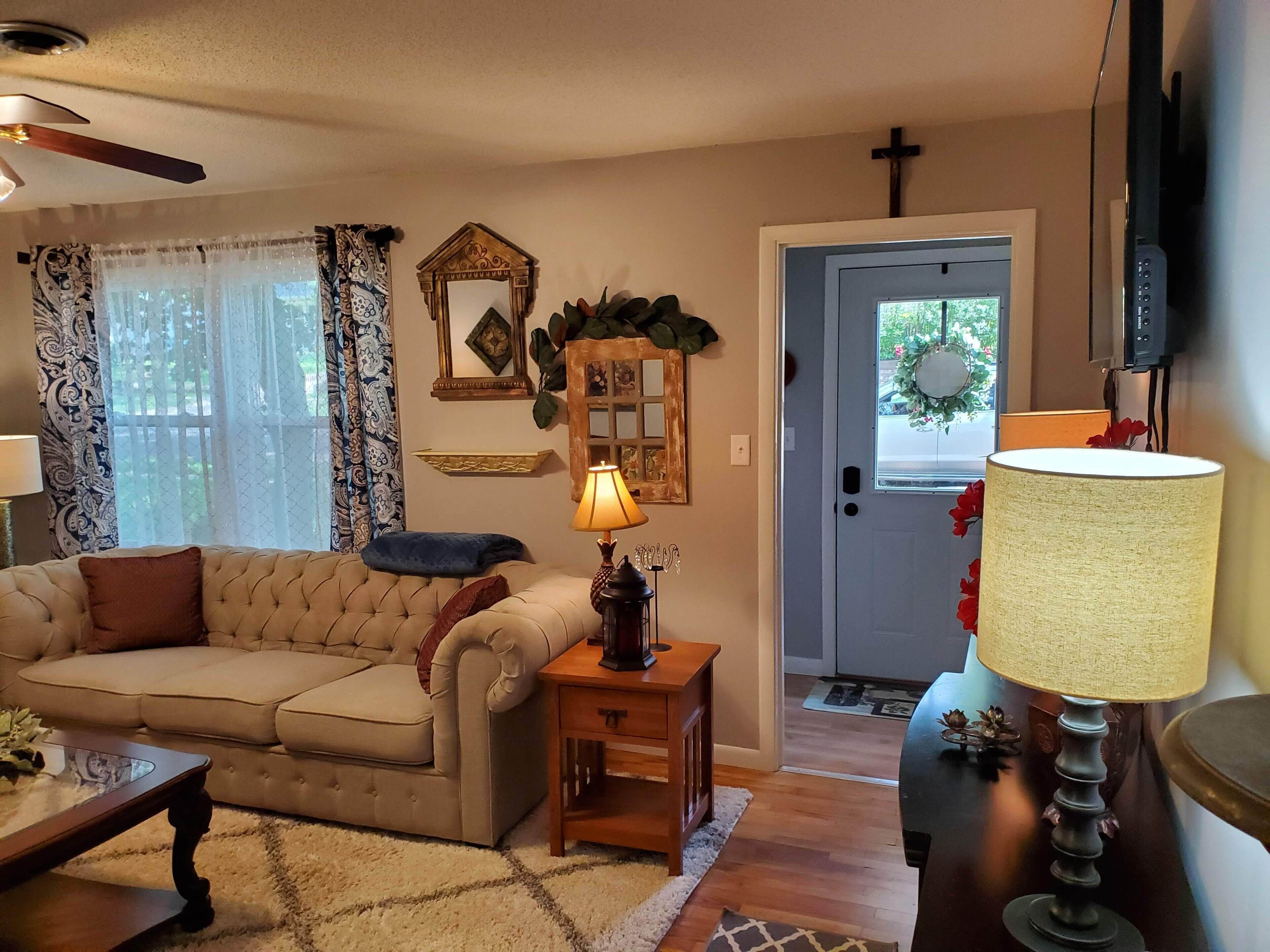 A living room with a beige sofa, a wooden coffee table, a lamp, and a door with a wreath.