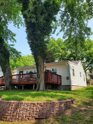 A single-story mobile home with a deck, surrounded by trees and a brick retaining wall. - Comfortable and relaxing Cottage getaway. (Saint Marys)