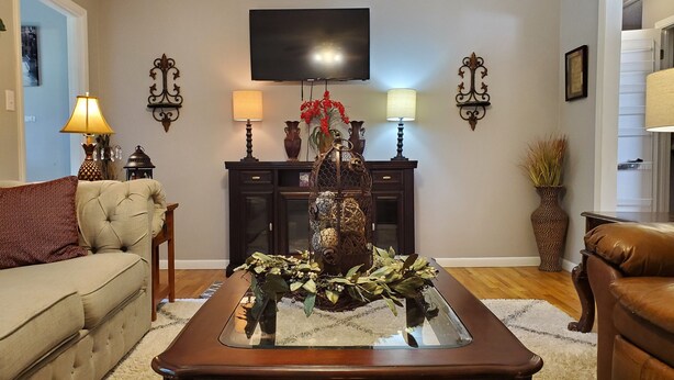A living room with a sofa, a coffee table with a decorative centerpiece, a TV mounted on the wall, and wall-mounted lamps. - Comfortable and relaxing Cottage getaway. (Saint Marys)