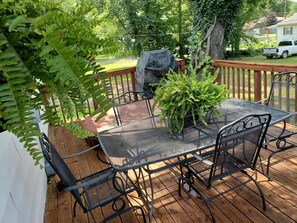 A wooden deck with a metal table and chairs, surrounded by greenery and a barbecue grill. - Comfortable and relaxing Cottage getaway. (Saint Marys)